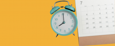 Türkiser Wecker und Kalender mit Juli-Monat auf gelbem Hintergrund – Symbolbild für rechtzeitige Planung und Vorbuchung auf dem Traumpfad München–Venedig