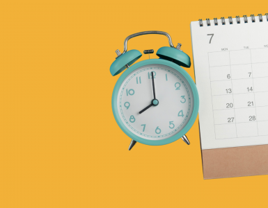 Türkiser Wecker und Kalender mit Juli-Monat auf gelbem Hintergrund – Symbolbild für rechtzeitige Planung und Vorbuchung auf dem Traumpfad München–Venedig