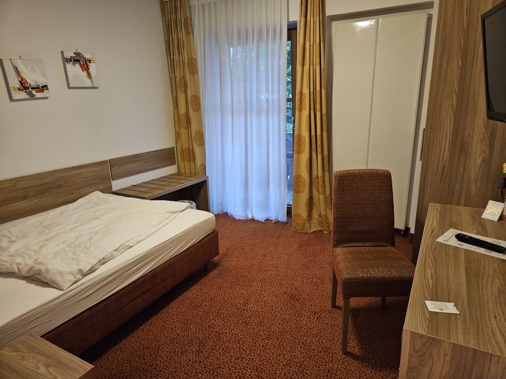 Helles Einzelzimmer mit Bett, Schreibtisch und Balkon im Isartaler Hof