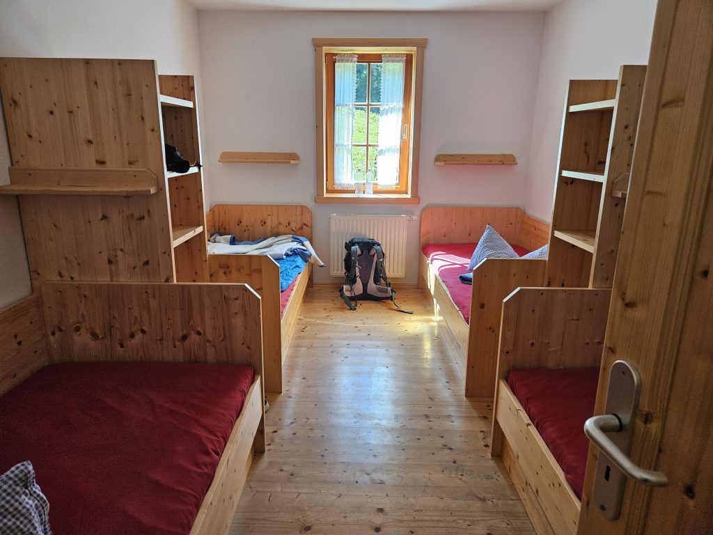 Einfaches Vierbettzimmer in der Tutzinger Hütte mit Holzbetten und Rucksack