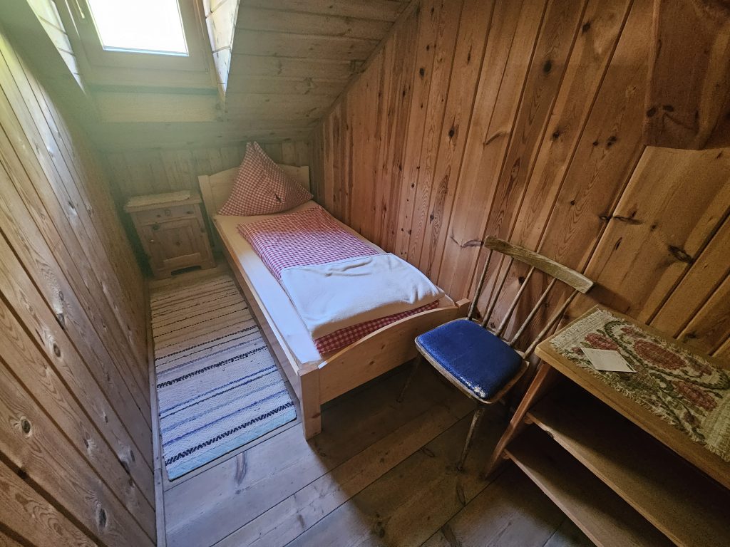 Kleines Einzelzimmer auf der Hallerangeralm mit Holzverkleidung, kariertem Bett und Tageslichtfenster