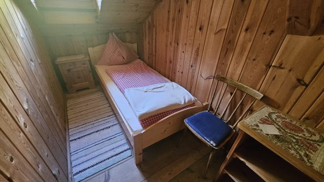 Kleines Einzelzimmer auf der Hallerangeralm mit Holzverkleidung, kariertem Bett und Tageslichtfenster