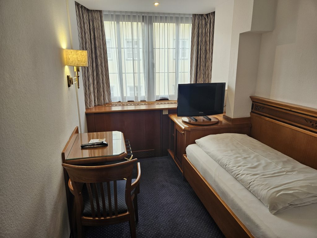 Einfaches Einzelzimmer im Hotel Mondschein mit Schreibtisch, Fernseher und großem Fenster
