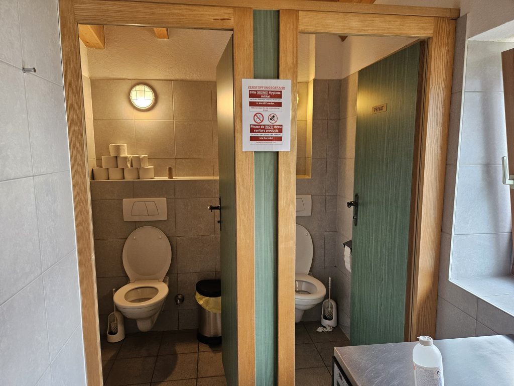 Zwei offene Toilettenkabinen in einem gefliesten Waschraum
