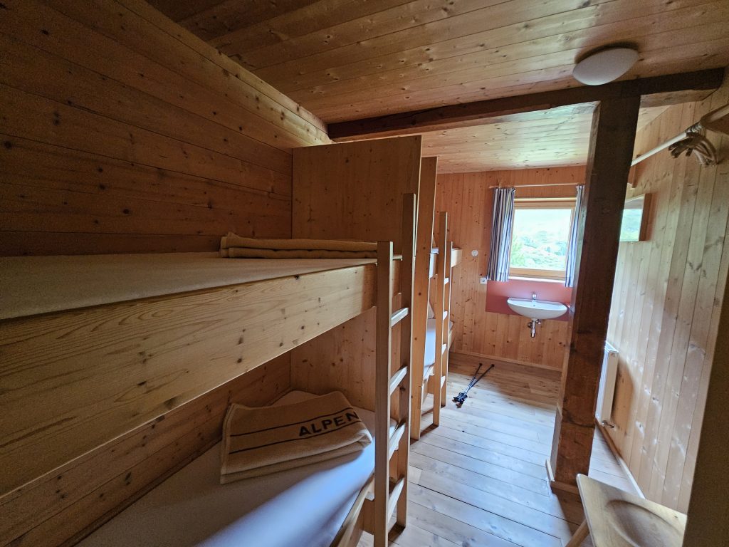 Holzverkleidetes Mehrbettzimmer mit Stockbetten und Waschbecken auf der Lizumer Hütte
