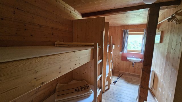 Holzverkleidetes Mehrbettzimmer mit Stockbetten und Waschbecken auf der Lizumer Hütte