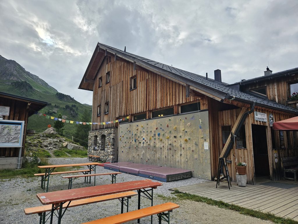 Holzhaus der Lizumer Hütte mit Kletterwand, Tischen und bunten Gebetsfahnen