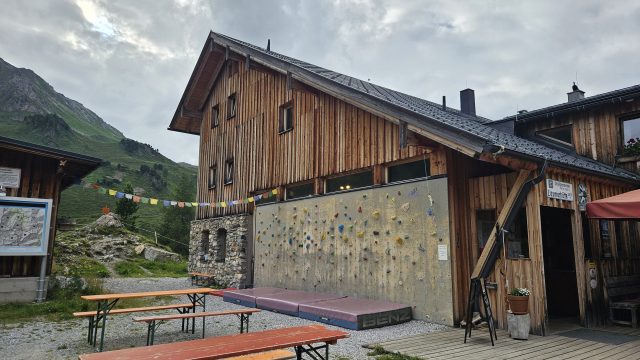 Holzhaus der Lizumer Hütte mit Kletterwand, Tischen und bunten Gebetsfahnen