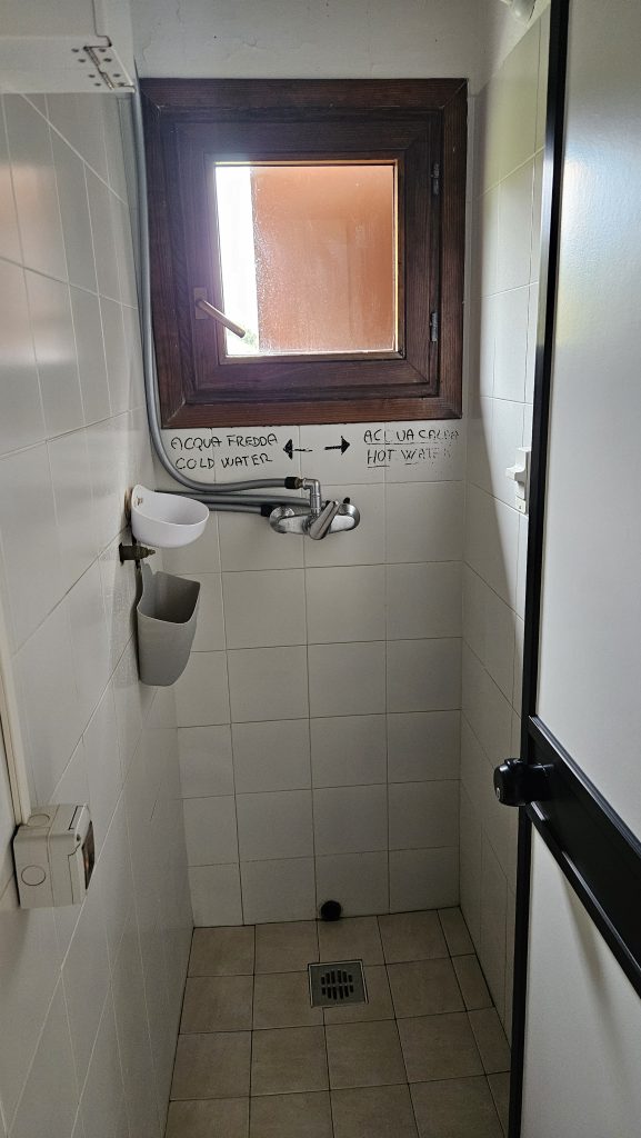 Enge Dusche mit markierten Warm- und Kaltwasserleitungen