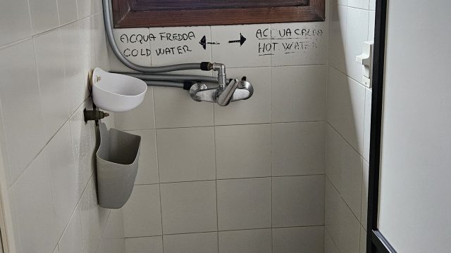 Enge Dusche mit markierten Warm- und Kaltwasserleitungen