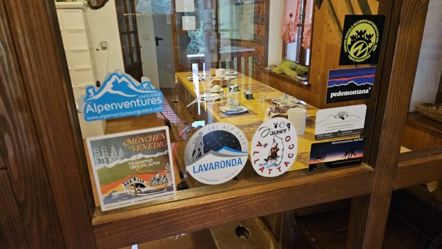 Blick durch die Glastür in den Frühstücksraum der Rifugio Bianchet mit Stickern zum München–Venedig-Traumpfad